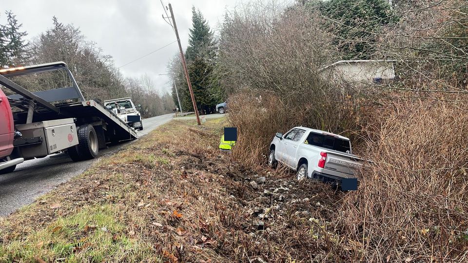 A pickup below the road, with tow equipment at the scene.